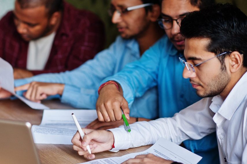Group of four south asian men's posed at business meeting in cafe. Indians together and sign important documents. Contract to study and work.