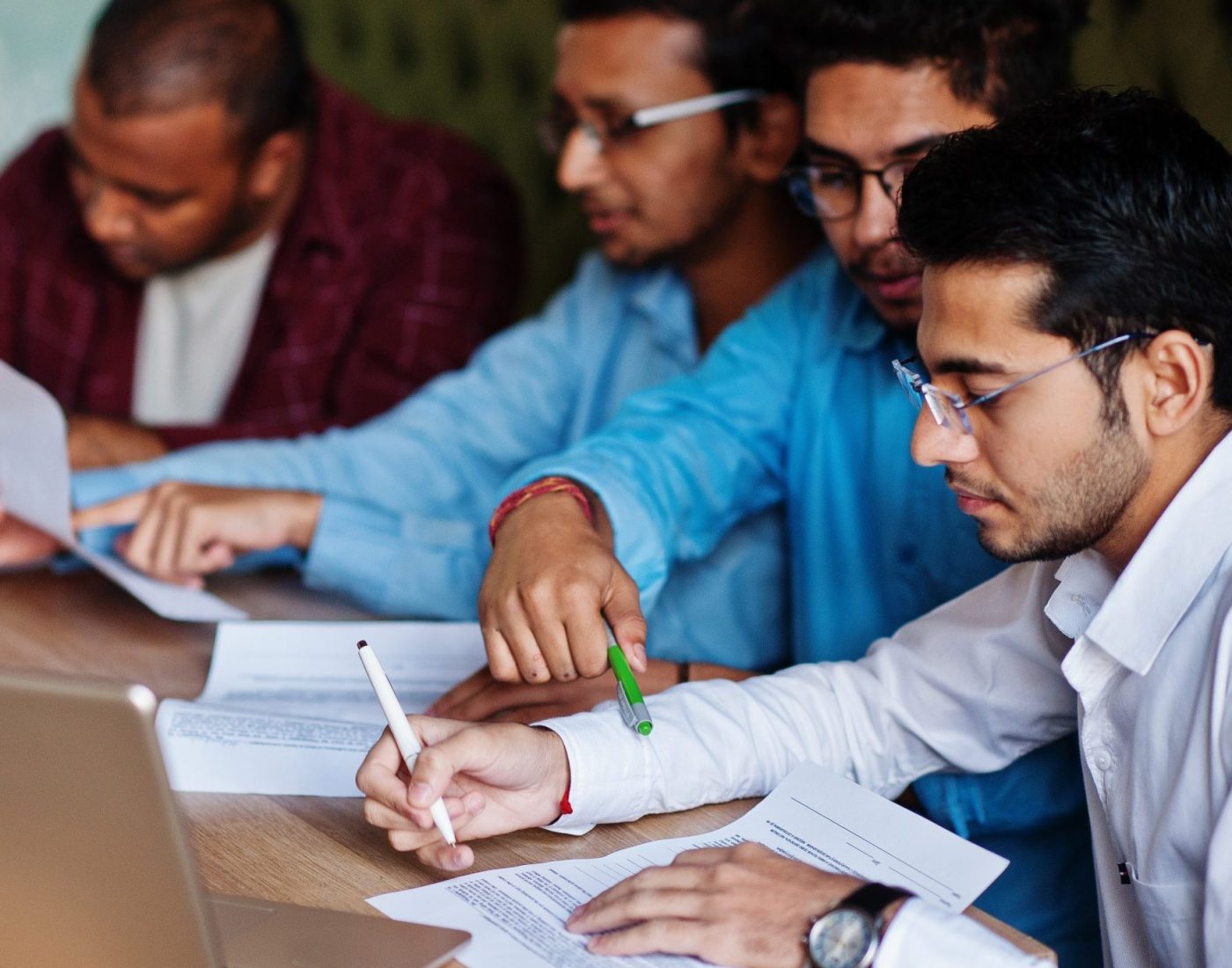 Group of four south asian men's posed at business meeting in cafe. Indians together and sign important documents. Contract to study and work.